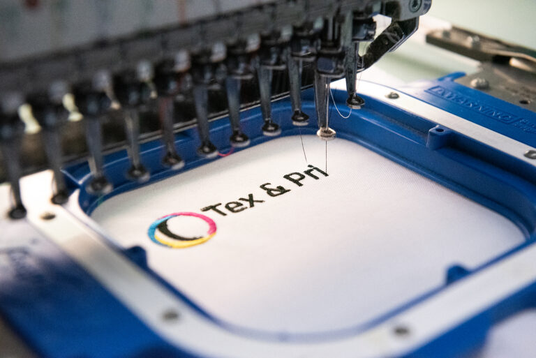 Tex & Print Logo wird im Stickrahmen auf weißen Stoff gestickt